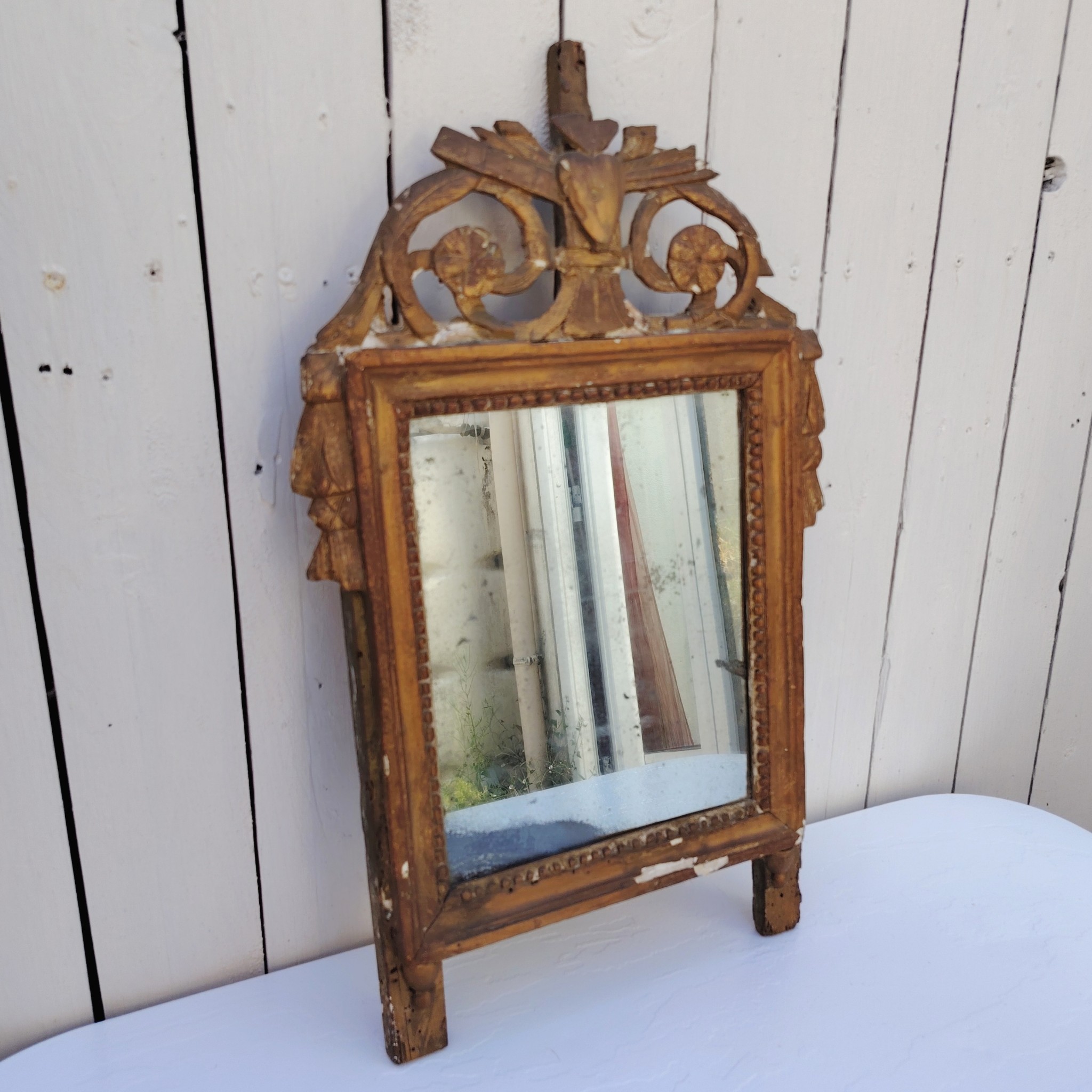 Ancien miroir en bois et stuc doré, de style Louis XVI, fin XVIIIéme début XIXéme. Fronton à enroulement de feuillage orné d'un coeur en son centre. Manque une partie du fronton, des éclats et maque de dorure. Tain terni et taché. Dans son jus Dimensions : 54 x 33 x 4 cm