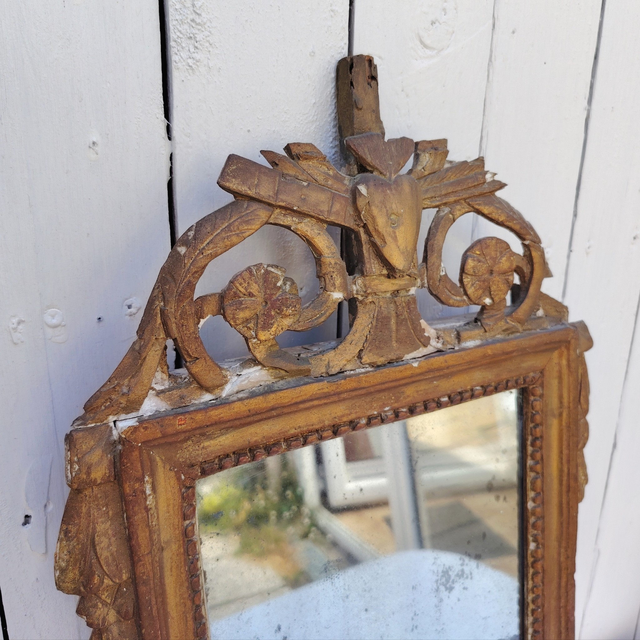 Ancien miroir en bois et stuc doré, de style Louis XVI, fin XVIIIéme début XIXéme. Fronton à enroulement de feuillage orné d'un coeur en son centre. Manque une partie du fronton, des éclats et maque de dorure. Tain terni et taché. Dans son jus Dimensions : 54 x 33 x 4 cm