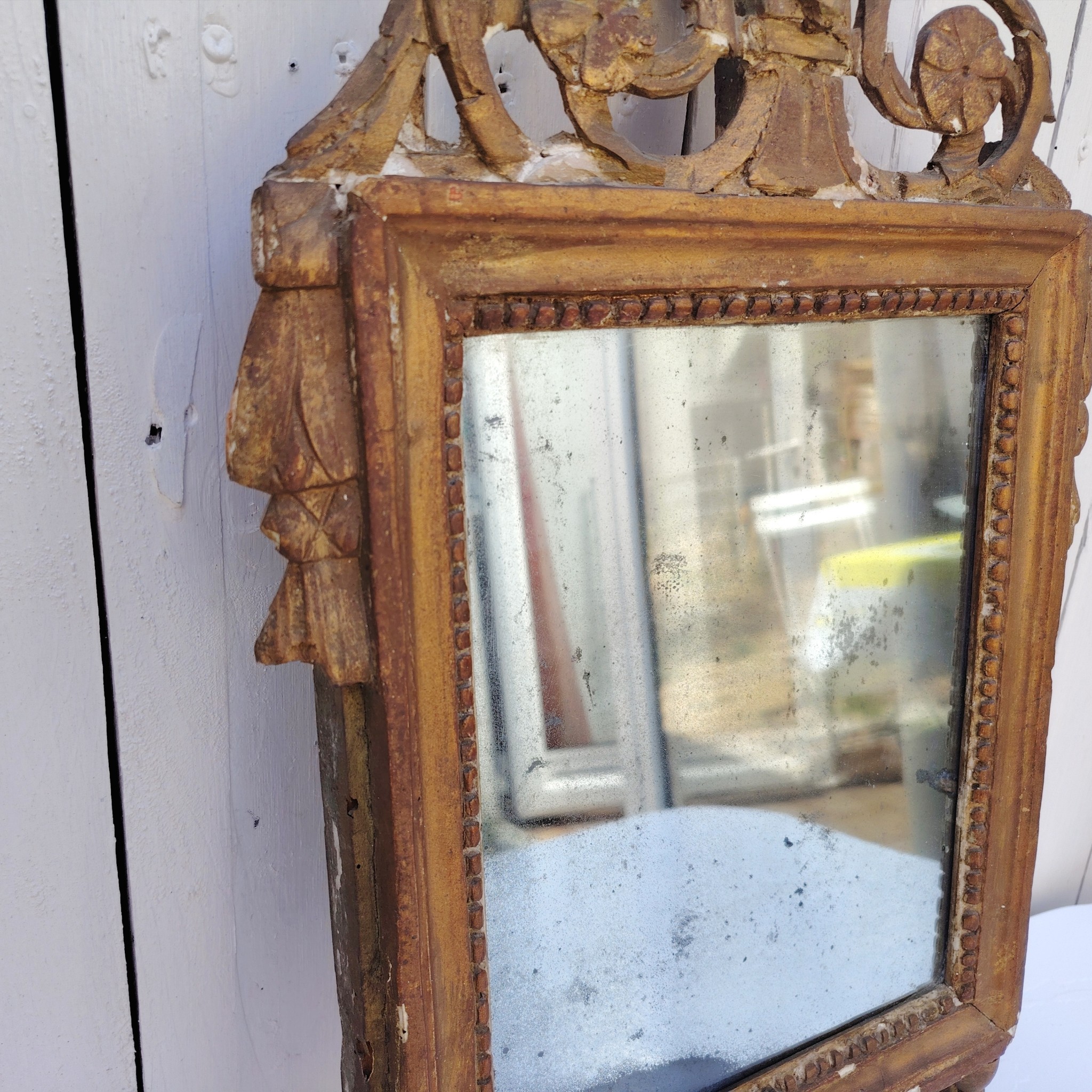 Ancien miroir en bois et stuc doré, de style Louis XVI, fin XVIIIéme début XIXéme. Fronton à enroulement de feuillage orné d'un coeur en son centre. Manque une partie du fronton, des éclats et maque de dorure. Tain terni et taché. Dans son jus Dimensions : 54 x 33 x 4 cm