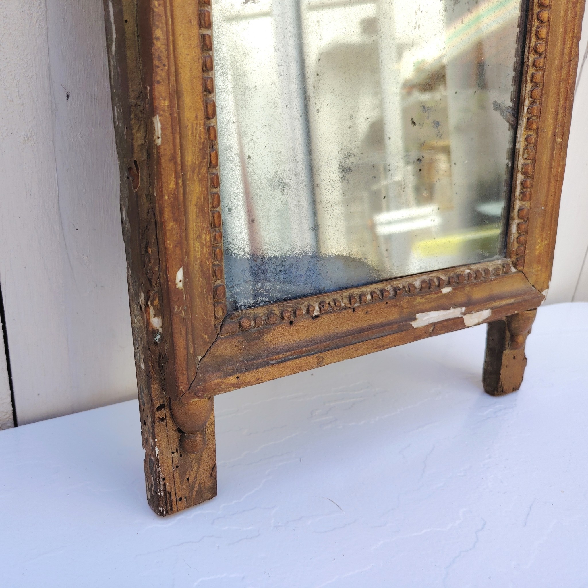 Ancien miroir en bois et stuc doré, de style Louis XVI, fin XVIIIéme début XIXéme. Fronton à enroulement de feuillage orné d'un coeur en son centre. Manque une partie du fronton, des éclats et maque de dorure. Tain terni et taché. Dans son jus Dimensions : 54 x 33 x 4 cm