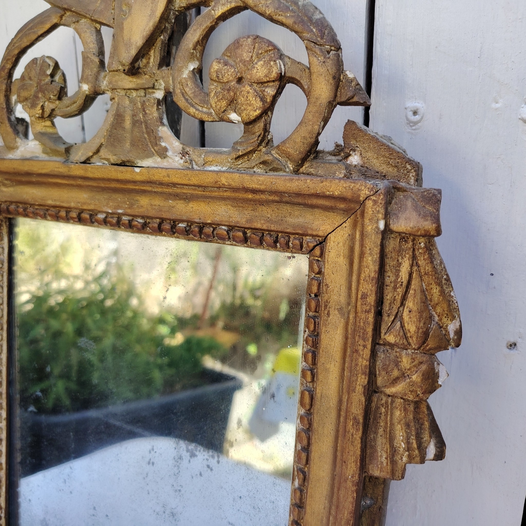 Ancien miroir en bois et stuc doré, de style Louis XVI, fin XVIIIéme début XIXéme. Fronton à enroulement de feuillage orné d'un coeur en son centre. Manque une partie du fronton, des éclats et maque de dorure. Tain terni et taché. Dans son jus Dimensions : 54 x 33 x 4 cm