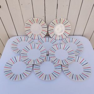 Lot de 10 assiettes à dessert en faïence de Longchamp, datant des années 50-60. Au décor de rayures colorées. Traces et rayures d'usage sans gravité, Un éclat sur le dessous de deux assiettes, non visible une fois posées Bon état général. Diamètre : 21 cm