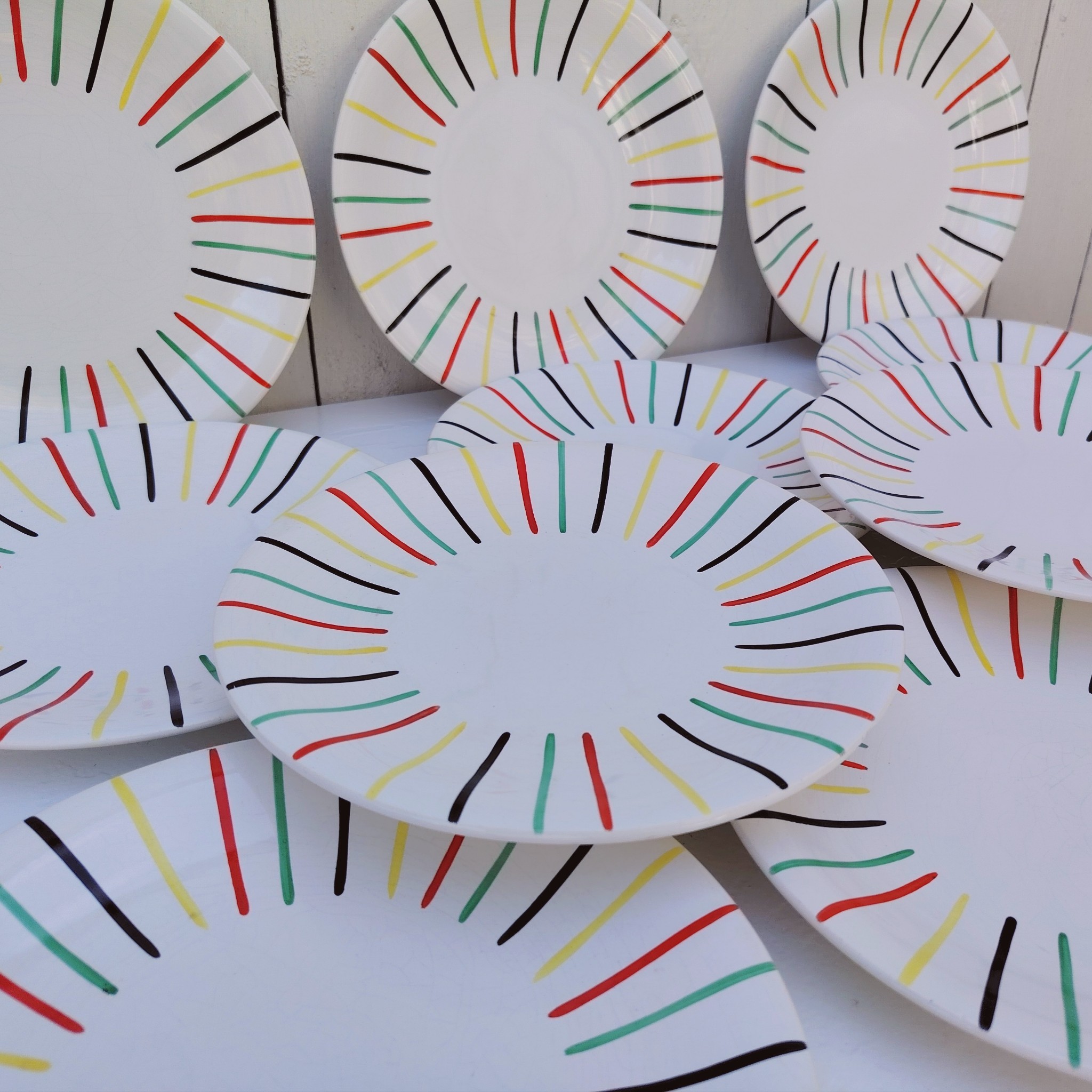 Lot de 10 assiettes à dessert en faïence de Longchamp, datant des années 50-60. Au décor de rayures colorées. Traces et rayures d'usage sans gravité, Un éclat sur le dessous de deux assiettes, non visible une fois posées Bon état général. Diamètre : 21 cm