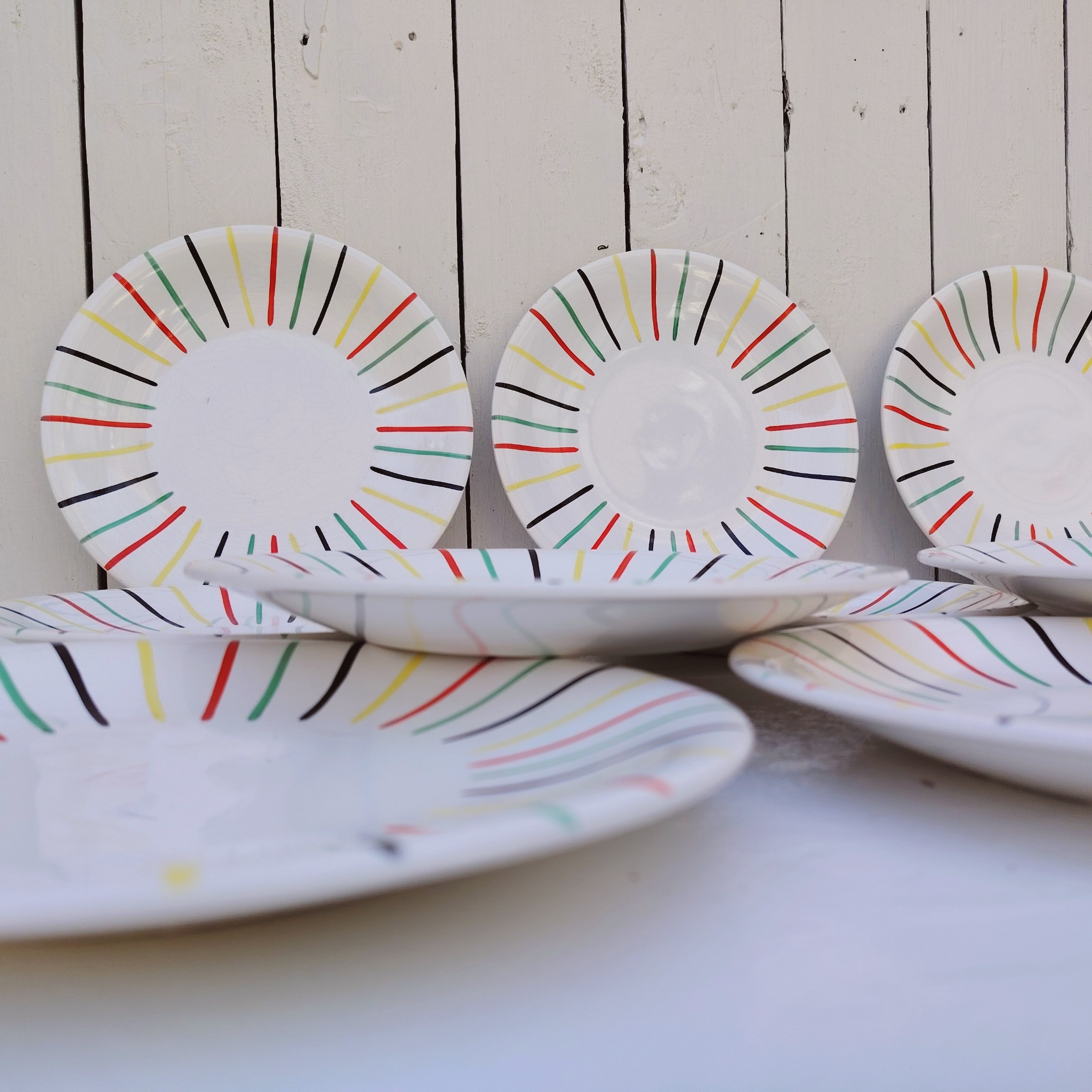 Lot de 10 assiettes à dessert en faïence de Longchamp, datant des années 50-60. Au décor de rayures colorées. Traces et rayures d'usage sans gravité, Un éclat sur le dessous de deux assiettes, non visible une fois posées Bon état général. Diamètre : 21 cm