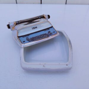 Boite à trombones en porcelaine de Limoges, à la forme de machine à écrire. Peut aussi servir de baguier ou porte cartes de visite. Cachet sur le dessous. Très bon état Dimensions :  9 x 10 x 5,5 cm