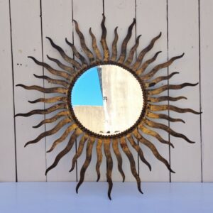 Miroir soleil, oeil de sorcière, en métal patiné doré datant des années 50. Miroir biseauté. Traces de corrosion et manques de dorures. Un point d'accroche sur l'arrière. Bon état général Diamètre total : 53,5 cm Diamètre miroir : 20,5 cm
