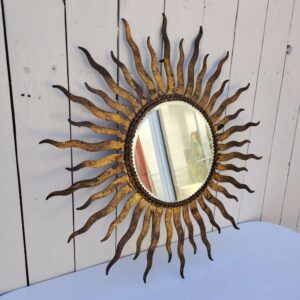 Miroir soleil, oeil de sorcière, en métal patiné doré datant des années 50. Miroir biseauté. Traces de corrosion et manques de dorures. Un point d'accroche sur l'arrière. Bon état général Diamètre total : 53,5 cm Diamètre miroir : 20,5 cm