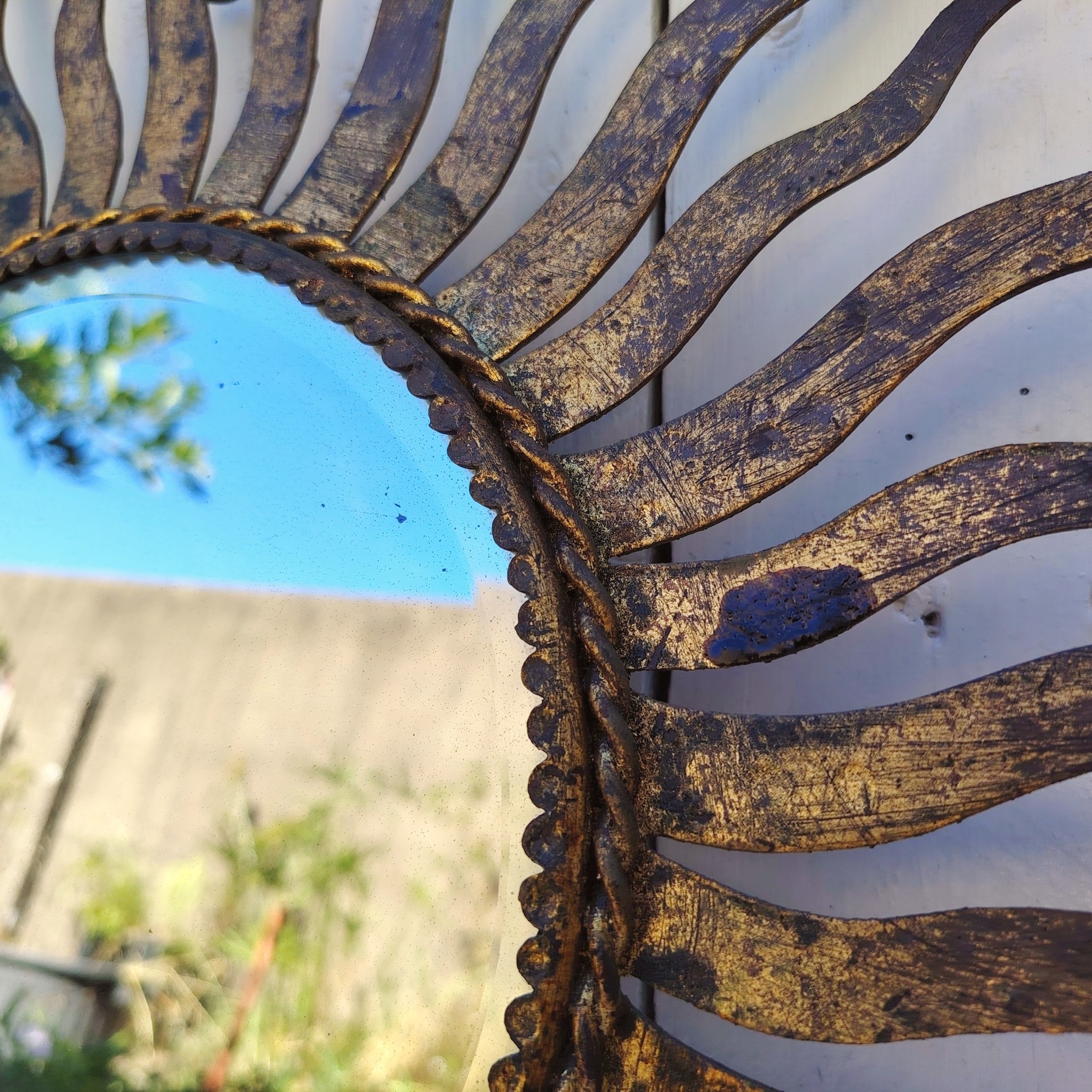 Miroir soleil, oeil de sorcière, en métal patiné doré datant des années 50. Miroir biseauté. Traces de corrosion et manques de dorures. Un point d'accroche sur l'arrière. Bon état général Diamètre total : 53,5 cm Diamètre miroir : 20,5 cm