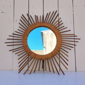 Miroir soleil en rotin datant des années 60. Traces de piqûres sur le miroir. Un point d'accroche sur l'arrière. Bon état général. Diamètre total : 42 cm Diamètre miroir : 17,5 cm