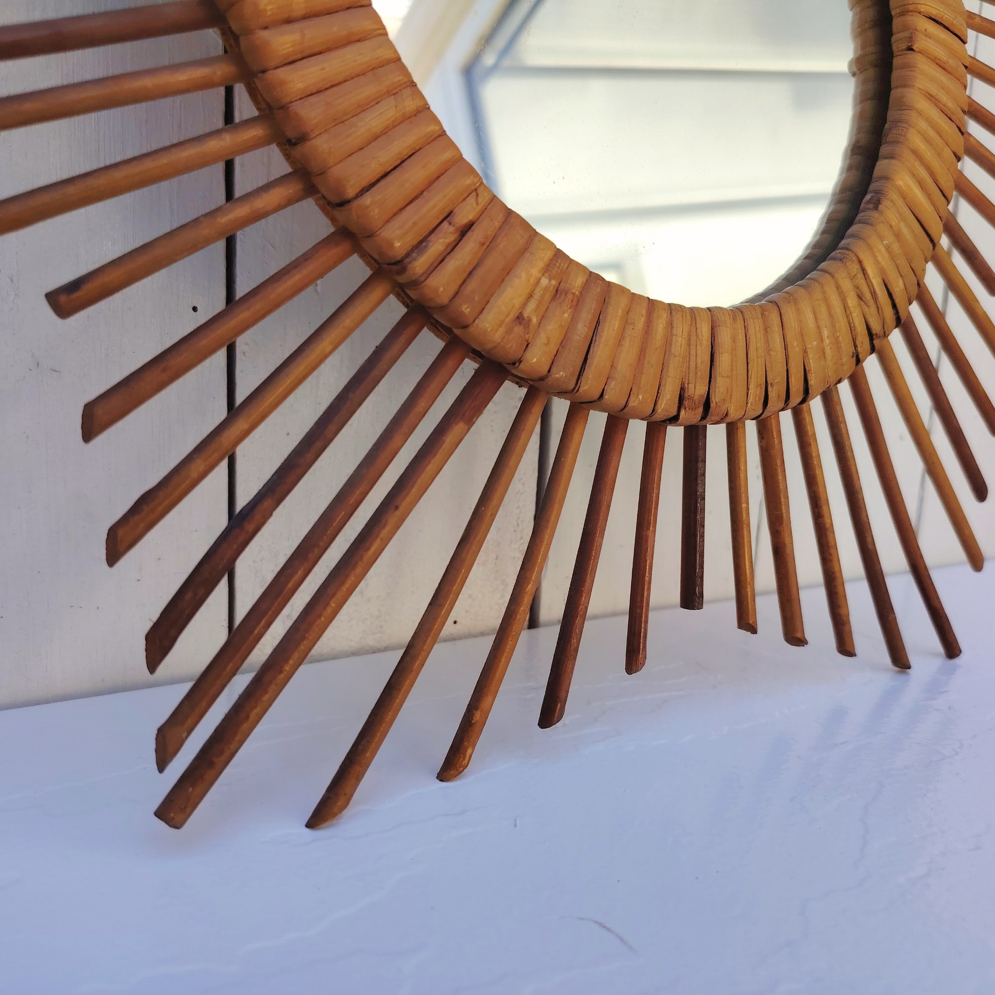  Miroir soleil en rotin datant des années 60.  Traces de  piqûres sur le miroir. Un point d'accroche sur l'arrière.  Bon état général. Diamètre total : 42  cm Diamètre miroir : 17,5 cm