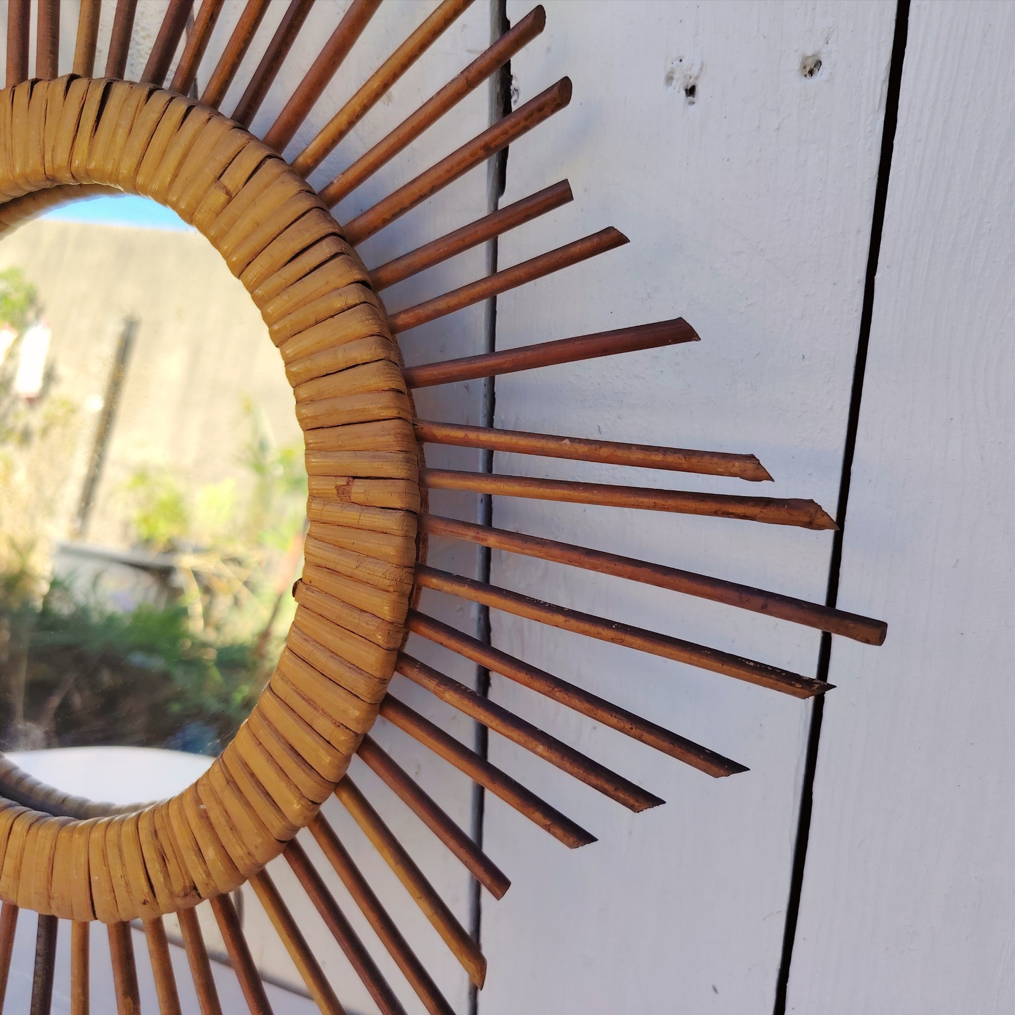  Miroir soleil en rotin datant des années 60.  Traces de  piqûres sur le miroir. Un point d'accroche sur l'arrière.  Bon état général. Diamètre total : 42  cm Diamètre miroir : 17,5 cm
