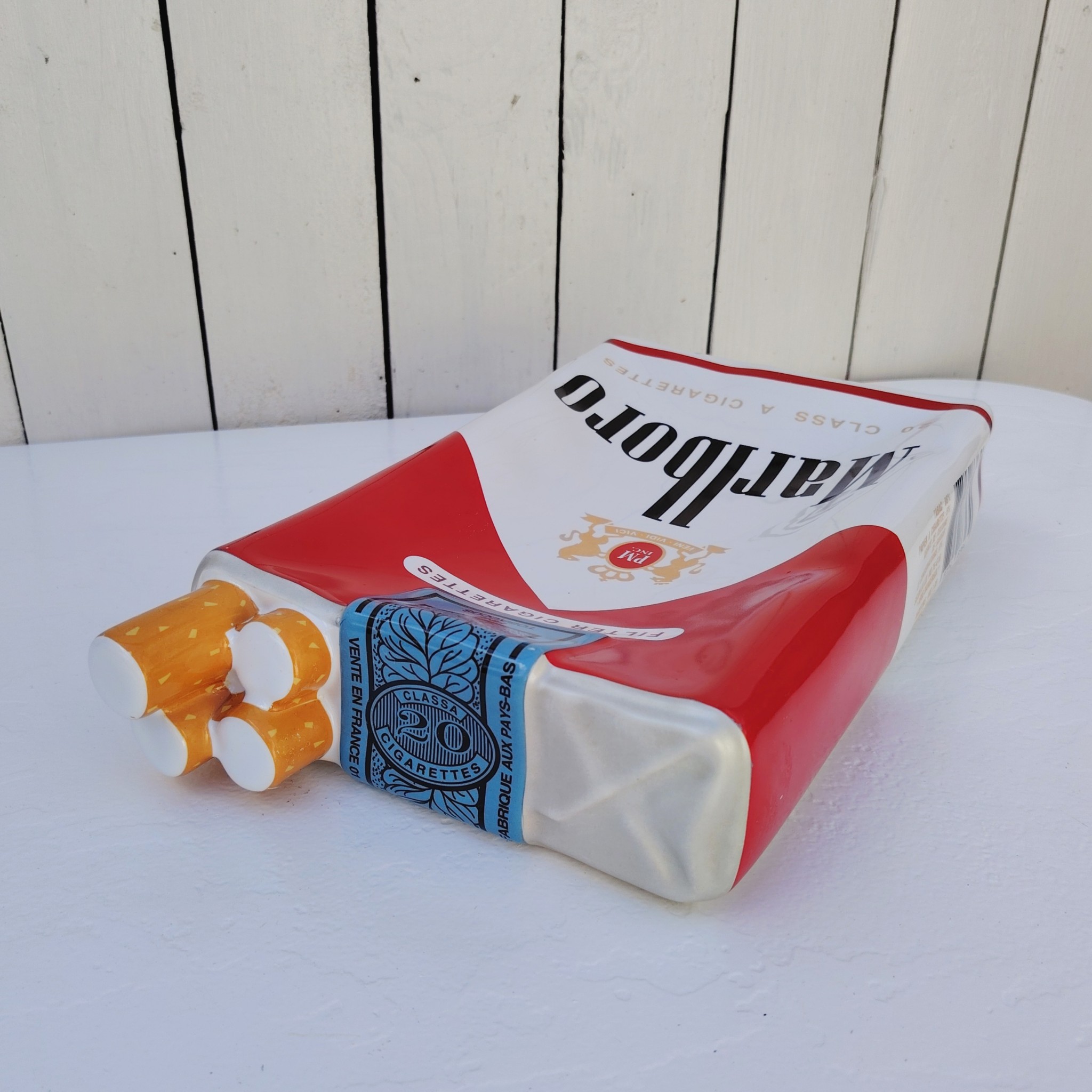 Grand vide poche en céramique représentant un paquet de cigarettes de la marque Marlboro. Petites rayures et traces d'usage sans gravité. Bon état général. Dimensions : 33 x 18 x 7 cm