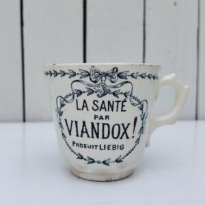  Rare tasse publicitaire VIANDOX en demi-porcelaine de Badonviller, ornée du slogan « La Santé par Viandox ! Produit Liebig ».   Décor bleu-vert, encadré de guirlandes végétales Cachet de la faïencerie de Badonviller sur le dessous, identifiable à sa marque à la couronne, confirmant une fabrication française  vers 1920.  Des petites égrenures sur le col  Bon état général Hauteur : 8 cm Diamètre : 8,5 cm