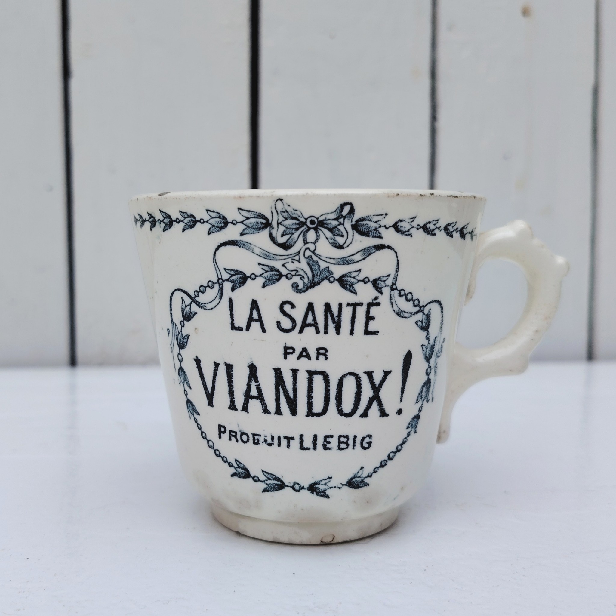 Rare tasse publicitaire VIANDOX en demi-porcelaine de Badonviller, ornée du slogan « La Santé par Viandox ! Produit Liebig ». Décor bleu-vert, encadré de guirlandes végétales Cachet de la faïencerie de Badonviller sur le dessous, identifiable à sa marque à la couronne, confirmant une fabrication française vers 1920. Des petites égrenures sur le col Bon état général Hauteur : 8 cm Diamètre : 8,5 cm