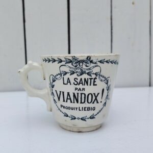  Rare tasse publicitaire VIANDOX en demi-porcelaine de Badonviller, ornée du slogan « La Santé par Viandox ! Produit Liebig ».   Décor bleu-vert, encadré de guirlandes végétales Cachet de la faïencerie de Badonviller sur le dessous, identifiable à sa marque à la couronne, confirmant une fabrication française  vers 1920.  Des petites égrenures sur le col  Bon état général Hauteur : 8 cm Diamètre : 8,5 cm