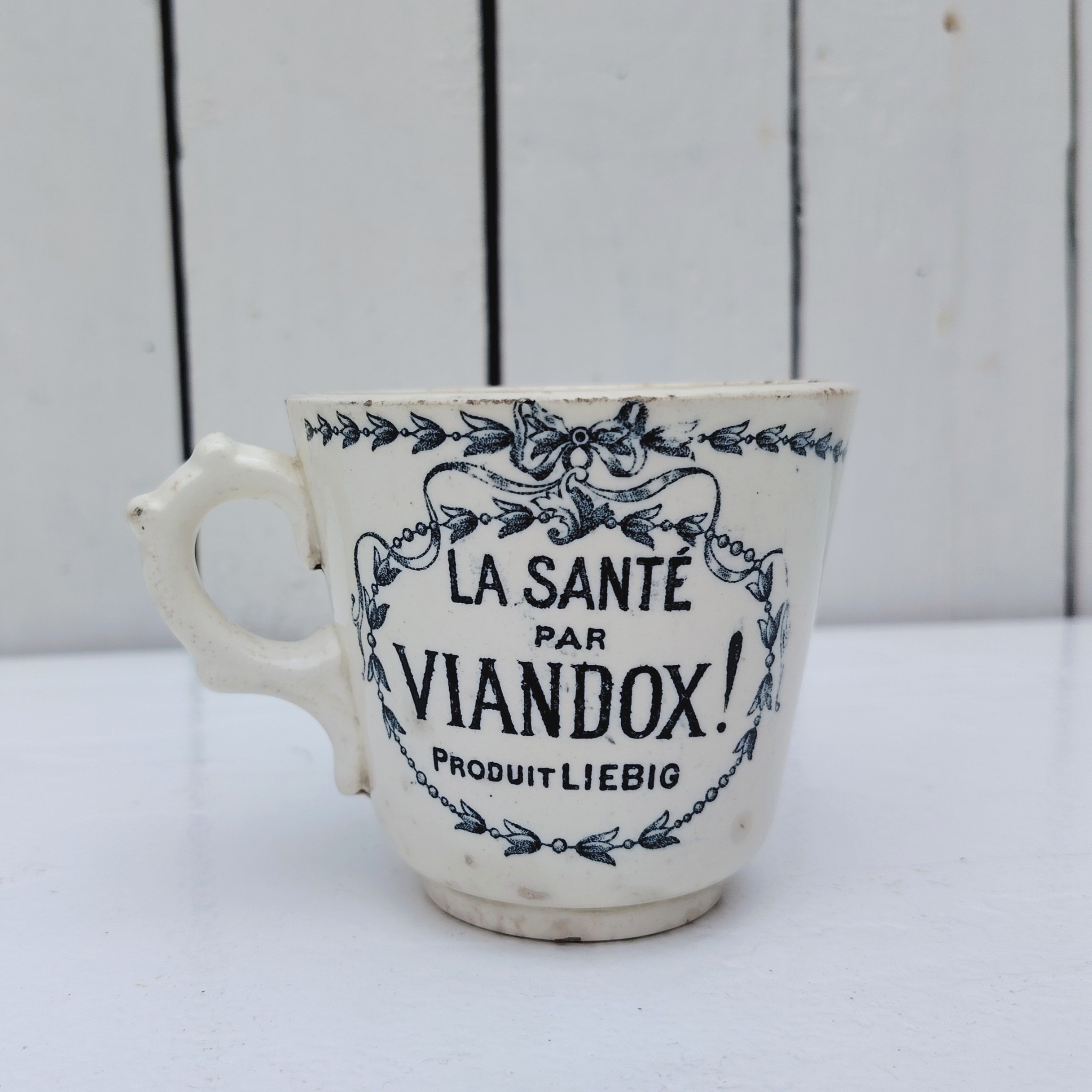 Rare tasse publicitaire VIANDOX en demi-porcelaine de Badonviller, ornée du slogan « La Santé par Viandox ! Produit Liebig ». Décor bleu-vert, encadré de guirlandes végétales Cachet de la faïencerie de Badonviller sur le dessous, identifiable à sa marque à la couronne, confirmant une fabrication française vers 1920. Des petites égrenures sur le col Bon état général Hauteur : 8 cm Diamètre : 8,5 cm