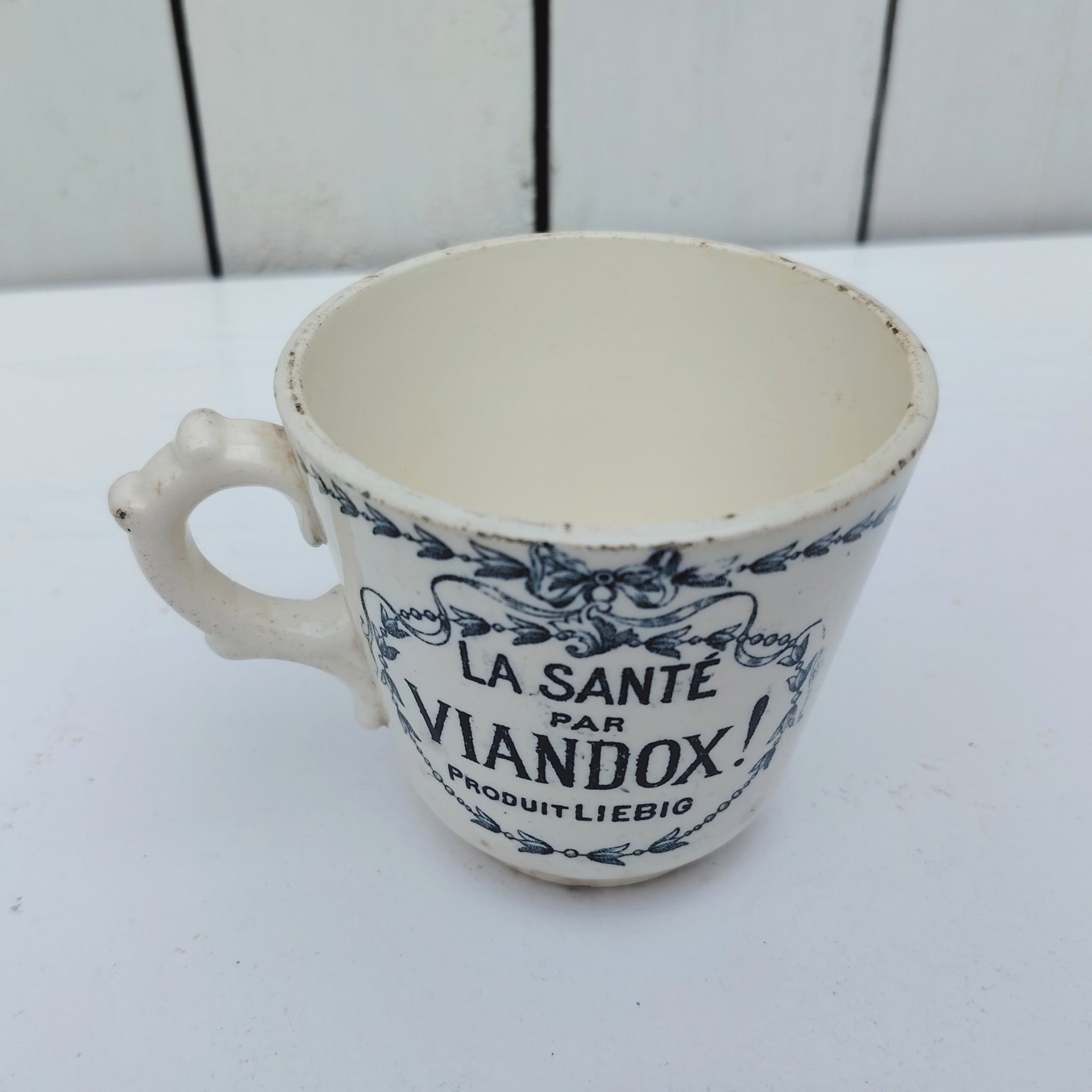 Rare tasse publicitaire VIANDOX en demi-porcelaine de Badonviller, ornée du slogan « La Santé par Viandox ! Produit Liebig ». Décor bleu-vert, encadré de guirlandes végétales Cachet de la faïencerie de Badonviller sur le dessous, identifiable à sa marque à la couronne, confirmant une fabrication française vers 1920. Des petites égrenures sur le col Bon état général Hauteur : 8 cm Diamètre : 8,5 cm