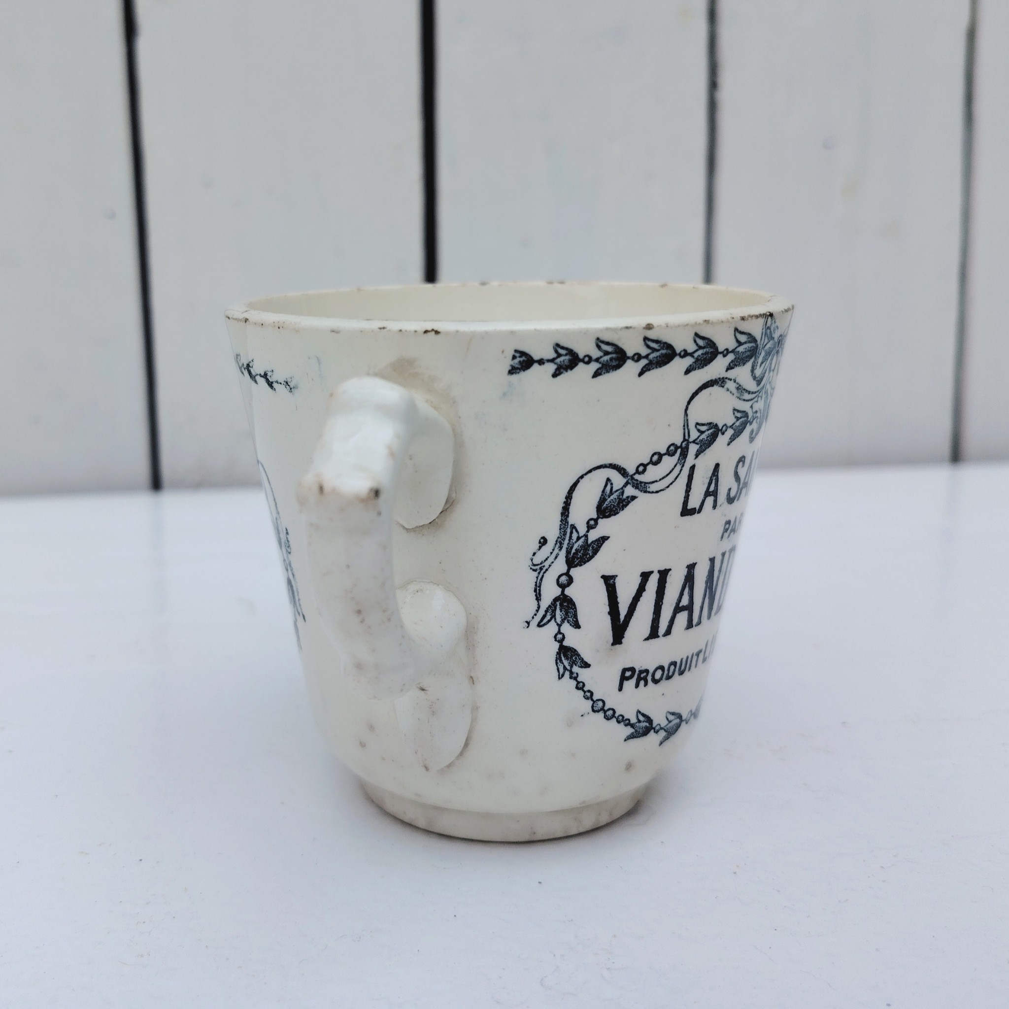 Rare tasse publicitaire VIANDOX en demi-porcelaine de Badonviller, ornée du slogan « La Santé par Viandox ! Produit Liebig ». Décor bleu-vert, encadré de guirlandes végétales Cachet de la faïencerie de Badonviller sur le dessous, identifiable à sa marque à la couronne, confirmant une fabrication française vers 1920. Des petites égrenures sur le col Bon état général Hauteur : 8 cm Diamètre : 8,5 cm