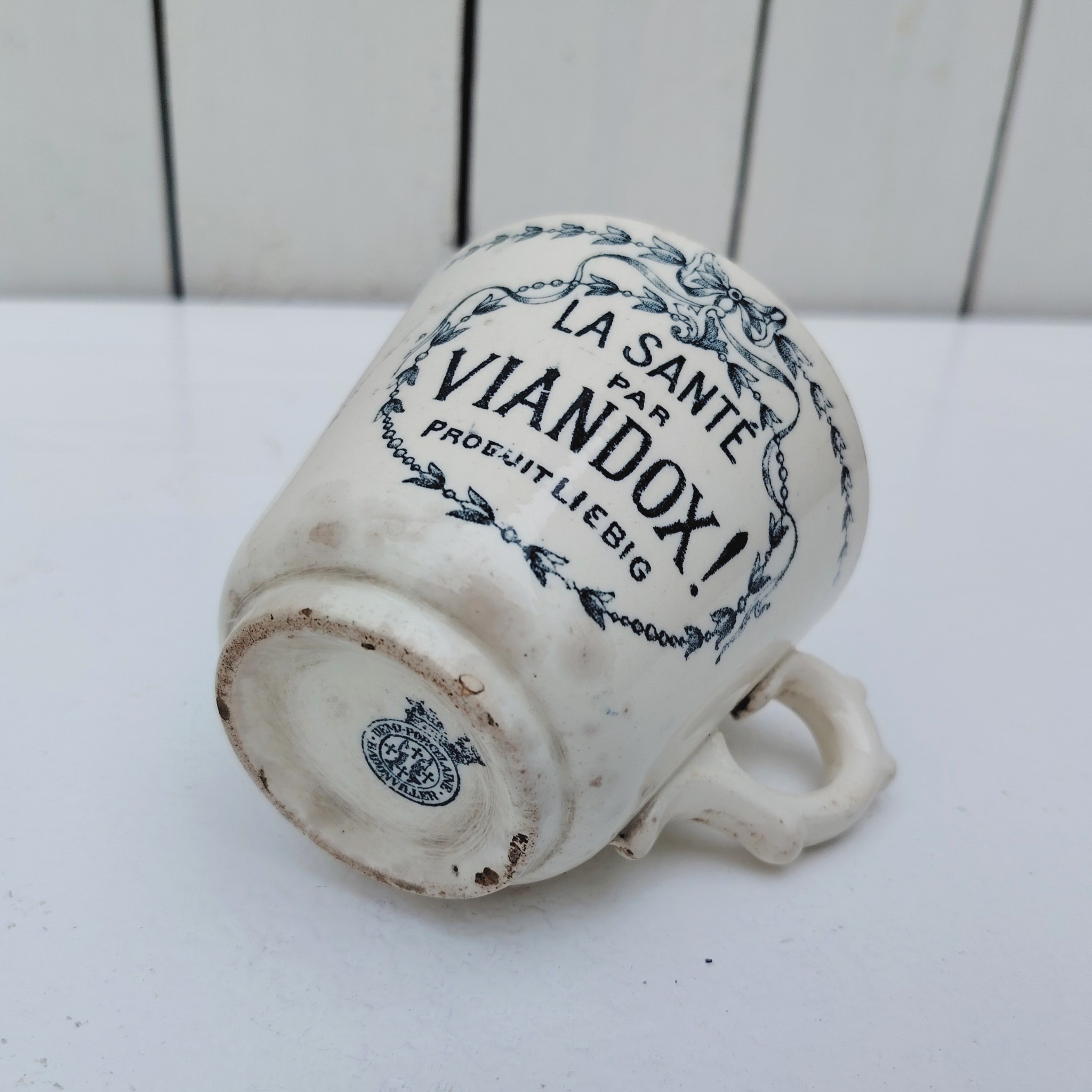 Rare tasse publicitaire VIANDOX en demi-porcelaine de Badonviller, ornée du slogan « La Santé par Viandox ! Produit Liebig ». Décor bleu-vert, encadré de guirlandes végétales Cachet de la faïencerie de Badonviller sur le dessous, identifiable à sa marque à la couronne, confirmant une fabrication française vers 1920. Des petites égrenures sur le col Bon état général Hauteur : 8 cm Diamètre : 8,5 cm